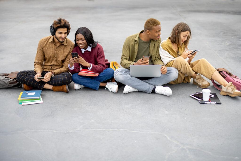 Students sitting and using smartphones on asphalt